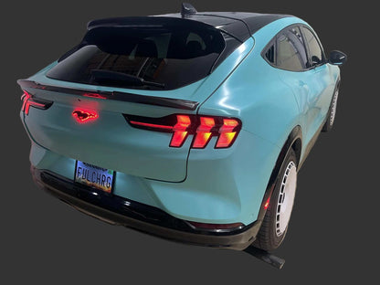 Rear view of a blue Mustang Mach-E with illuminated Light-Up Ponies emblem glowing red on the back.
